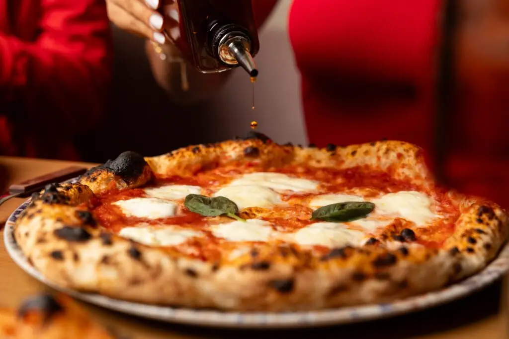 Neapolitanische Pizza mit Mozzarella und Basilikum, verfeinert mit Chili-Öl – im Hintergrund eine Frau im roten Oberteil