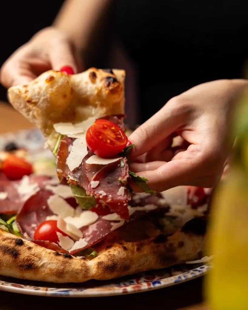 Ein Stück Pizza mit Rohschinken, Tomaten und Parmesan