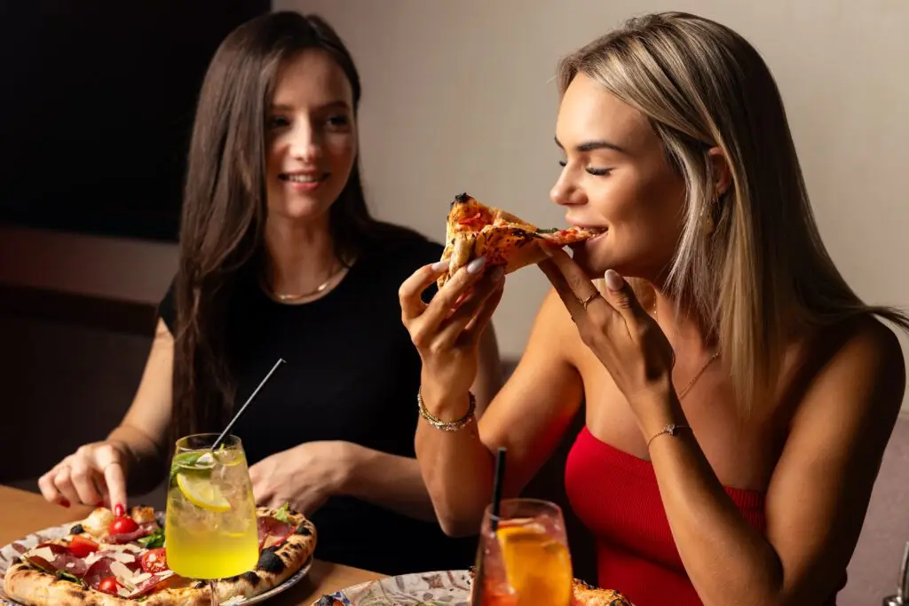 Zwei Frauen genießen neapolitanische Pizza und bunte Drinks in entspannter Atmosphäre