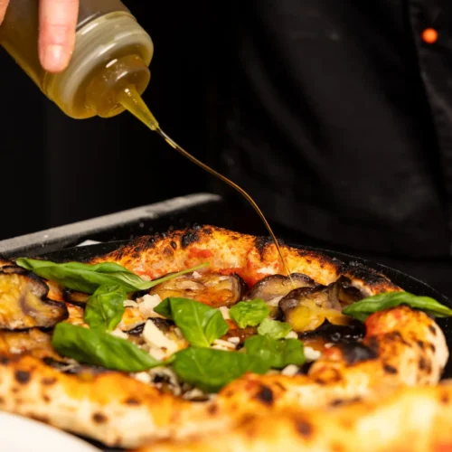 eine Pizza Mit Aubergine, Basilikum und Parmesan wird mit Olivenöl garniert